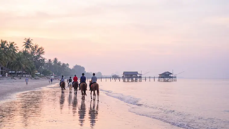 Chevaux sur la plage de Hua Hin au petit matin, maisons de pêcheurs sur pilotis