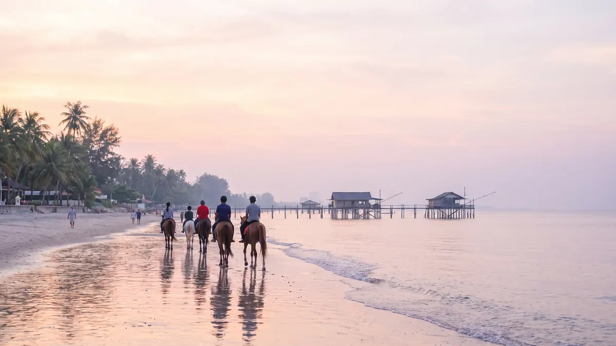 Chevaux sur la plage de Hua Hin au petit matin, maisons de pêcheurs sur pilotis